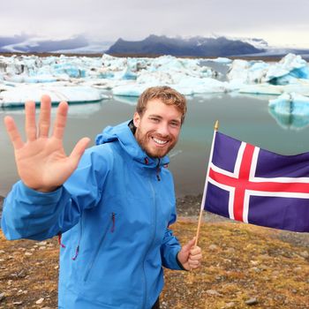 Iceland travel tourist showing Icelandic flag by Jokulsarlon. Man hiker happy holding showing Icelandic flag in front of the glacial lake / glacier lagoon. Happy male smiling in tourism concept.