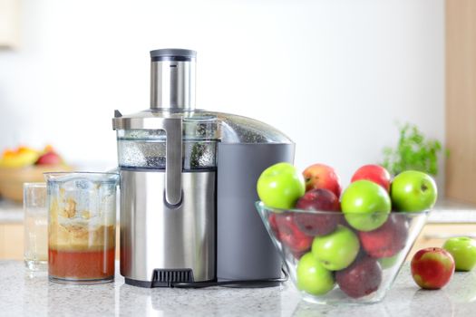 Apple juice on juicer machine - juicing concept. Apples in bowl in kitching and fresh pressed juice.