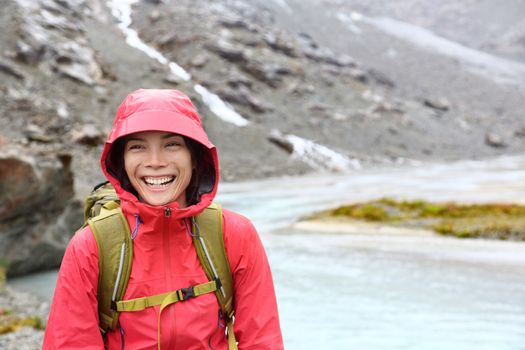 Hiker woman hiking with backpack in rain on trek living healthy active lifestyle. Smiling cheerful girl walking on hike in beautiful mountain nature landscape while raining in Swiss alps, Switzerland.