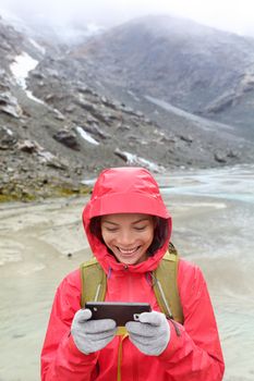 Smart phone woman texting sms using app on smartphone with touchscreen gloves. Happy hiker with mobile phone outside in nature in rain. Girl with glove of conductive fabric for touch screen.