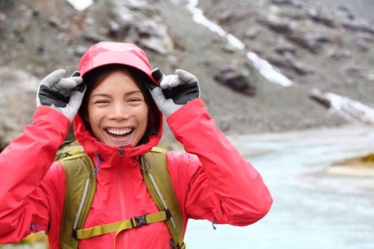 Laughing happy woman hiking with backpack in rain on trek living healthy active lifestyle. Smiling cheerful girl walking on hike in beautiful mountain nature landscape raining, Swiss alps, Switzerland