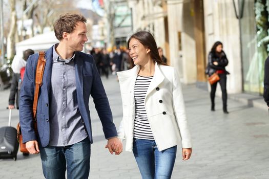 Urban modern professionals couple walking romantic laughing talking holding hands on date. Young multicultural couple Asian and Caucasian. From famous Passeig de Gracia, Barcelona, Catalonia, Spain.
