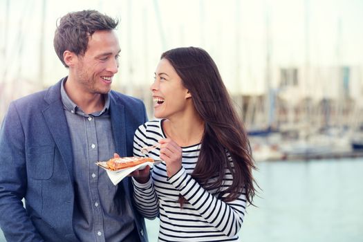 Dating couple tourists eating waffles on date enjoying food snack. Romantic man and woman laughing having fun outdoors. Multiracial couple, Young Caucasian man and Asian woman.