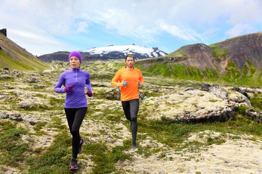 Sport running. Runners on cross country trail outdoors working out for marathon. Fit young fitness model man and asian woman training together outside in mountain nature on Snaefellsnes, Iceland.