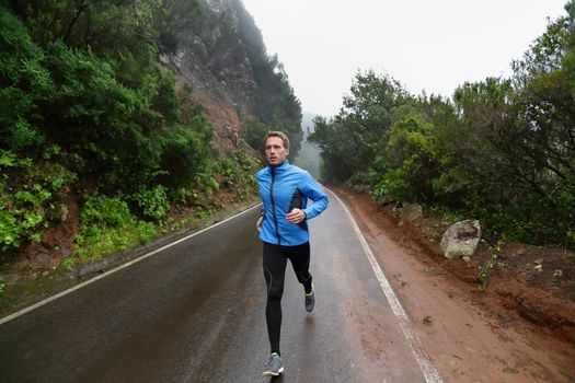 Male runner jogging and running on road in rain in jacket and long tights. Fit fitness model man working out living healthy lifestyle training for marathon. Young caucasian model in his 20s.