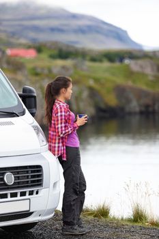 Travel woman by mobile motor home RV campervan. Traveler relaxing camping and enjoying traveling on Iceland in recreational vehicle. Girl enjoying coffee in Icelandic nature landscape.