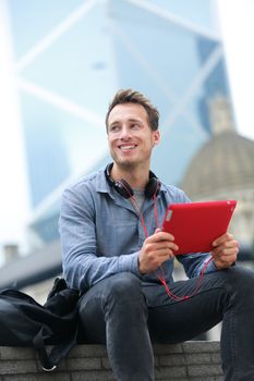 Urban young professional man using tablet computer sitting in Hong Kong outside using app on 4g wireless device wearing headphones. Casual young urban professional male in his late 20s.