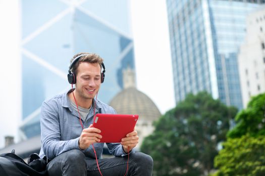 Man talking on tablet pc having video chat conversation in sitting outside using app on 4g wireless device wearing headphones. Casual young urban professional male in his late 20s. Hong Kong.
