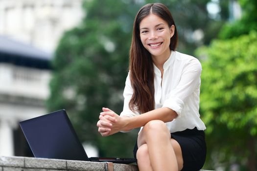 Business people - woman on laptop in Hong Kong. Businesswoman on computer and internet outside in Central Hong Kong. Young female professional business woman smiling. Asian Chinese Caucasian woman.