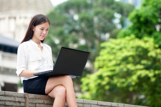 Business woman with computer laptop working outside looking at screen in business district, Central, Hong Kong. Young female professional businesswoman sitting outdoors. Asian Chinese Caucasian woman.
