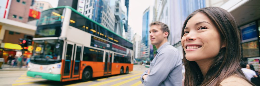 City people lifestyle banner of couple walking crossing the street with double decker bus driving down the road background. Panoramic landscape banner crop. Happy Asian woman, Caucasian man.