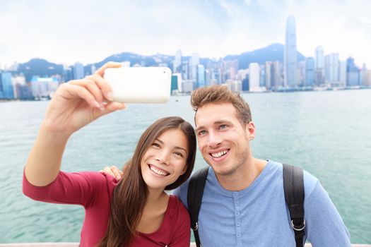 Selfie - friends taking self-portrait picture photo in Hong Kong enjoying sightseeing on Tsim Sha Tsui Promenade and Avenue of Stars in Victoria Harbour, Kowloon, Hong Kong. Travel concept.