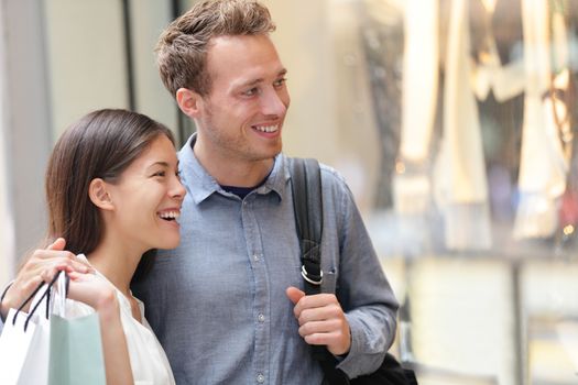 Couple shopping in Hong Kong Central looking at shop windows holding shopping bags. Urban mixed race Asian Chinese woman shopper and Caucasian man smiling happy living in city.