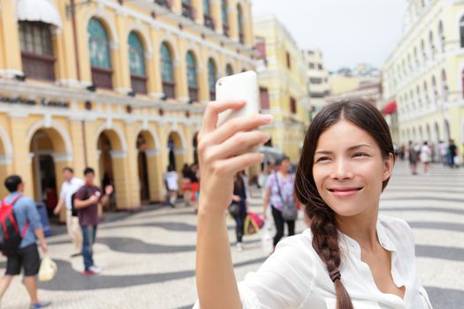 Woman tourist taking selfie pictures in Macau, China in Senado Square or Senate Square. Asian girl tourist using smart phone camera to take photo while traveling in Macau. Travel and tourism concept.