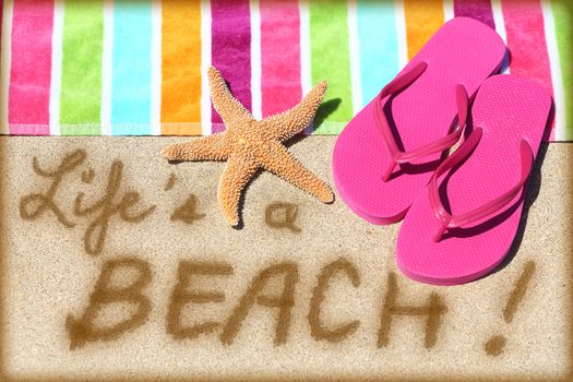 Beach travel fun sign. LIFE IS A BEACH written in sand with water next to beach towel, summer sandals and starfish. Summer and sun vacation holidays concept background.