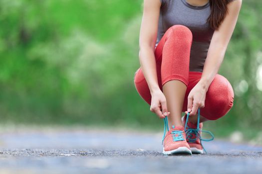 Running shoes - closeup of woman tying shoe laces. Female sport fitness runner getting ready for jogging outdoors on forest path in spring or summer.