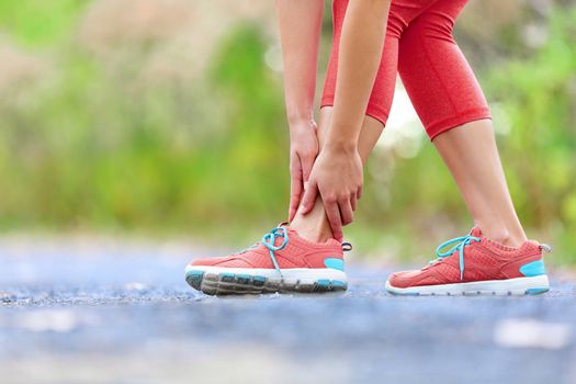 Twisted broken ankle - running sport injury. Female runner touching foot in pain due to sprained ankle.