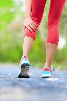 Muscle injury - woman running clutching calf muscle after spraining it while out jogging on the beach. Female athlete sport injury.