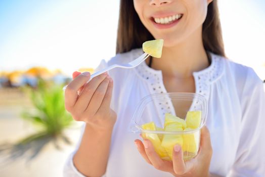 Pineapple - woman eating sliced Hawaiian pineapple fruit as a healthy snack from take away bowl.