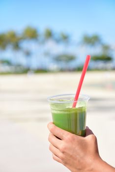 Green vegetable smoothie - healthy eating concept. Close up of green vegetable detox smoothie with spinach. Woman hand holding vegetable smoothies outside on summer beach.