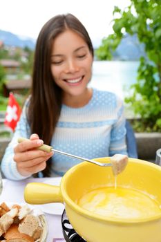 Cheese fondue - woman eating local Swiss food dipping bread in melted cheese. People eating traditional food from Switzerland having fun by lake in the Alps on travel in Europe.