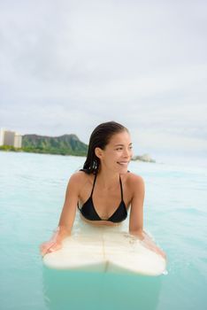 Surfing surfer girl looking for surf on surfboard. Female bikini woman living healthy active water sports lifestyle on Hawaiian beach. Asian Caucasian model on Waikiki Beach, Oahu, Hawaii.