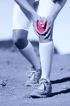 Greyscale image of the legs of a sportsman with a knee injury clasping his knee depicted in red selective color conceptual of a pulled muscle, cartridge, strain, sprain or tendon injury