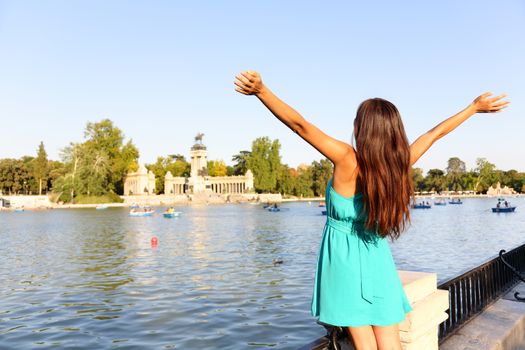 Happy success woman in Madrid park El Retiro. Successful girl cheerful with arms up outstretched in by lake Parque el Retiro in Madrid, Spain, Europe. Woman in summer dress.