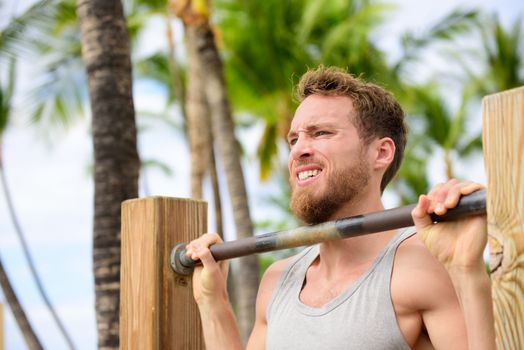 Crossfit man working out pull-ups on chin-up bar. Portrait of bearded fit young man cross training arms on horizontal bars outside on outdoor gym in summer.