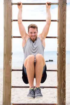 Fitness people - man training abs by lifting legs on cross fit bar rack outside on outdoor gym station.