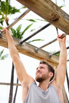 Workout fit man working out arm training on brachiation horizontal ladder or monkey bars in outside beach gym outdoors.