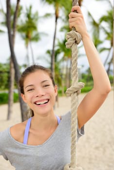 Fitness girl portrait - healthy fit woman smiling. Adorable mixed race asian chinese female athlete holding crossfit climbing rope on outdoor beach gym outside.