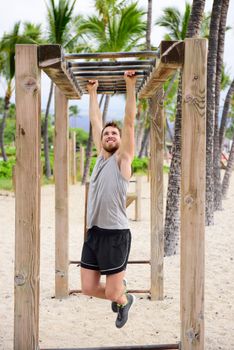 Fitness man on monkey bars fitness station gym. Strong male trainer training on brachiation ladder outdoors equipment as part of crossfit workout routine.