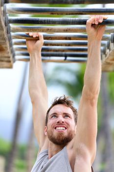 Fit man cross training on monkey bars station. Fitness workout on brachiation ladder in an outdoor gym outside. Male athlete swinging on high bars exercising.