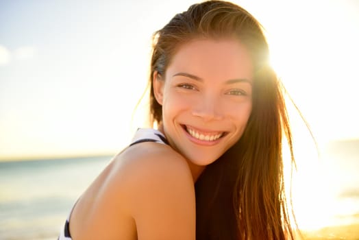 Asian beautiful girl smiling happy on beach vacation enjoying warm sunshine. Mixed race Asian Caucasian pretty model outside with sun in background on Hawaiian tropical beach.