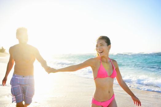 Young happy mixed race couple holding hands enjoying vacation travel honeymoon on sunny summer beach. Beautiful mixed race asian caucasian woman. Tropical Hawaii.