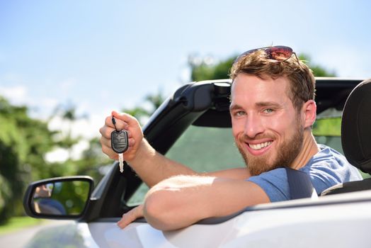 Man driving rental car showing new car keys happy. Young adult excited on road trip with key for cars leasing or rental or purchase.