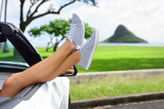 Relaxing vacation car road trip travel with feet up the window. Convertible car holiday concept with female legs in front of Oahu landmark : Chinaman's Hat in Hawaii, USA.