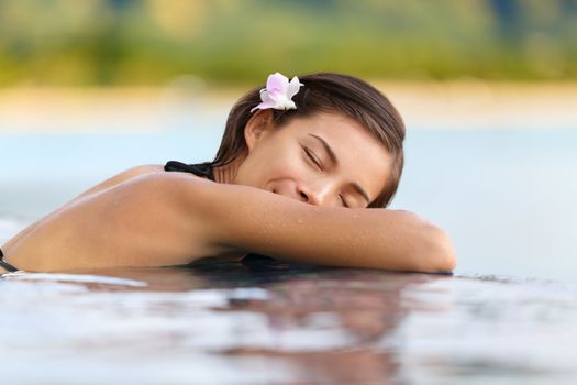 Relaxing woman in luxury hotel pool on holidays - vacation travel. Asian young female person sleeping in pool spa at hotel resort in an exotic getaway.