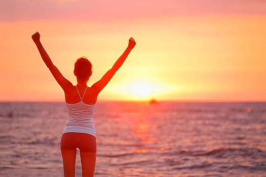 Happy cheering celebrating success woman at beautiful beach sunset. Fitness girl enjoying view with arms raised up towards the sky. Happy free freedom sport concept image outdoors.