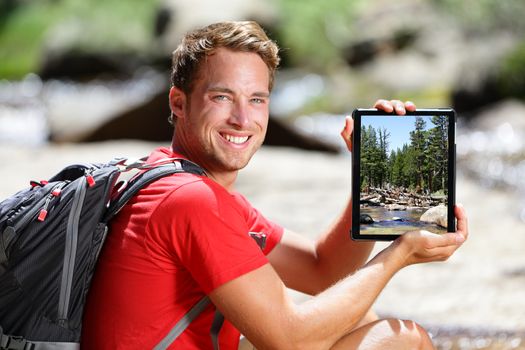 Hiking man showing nature forest picture on tablet. Young adult taking pictures with digital tablet computer of landscape in Yosemite National Park, California, USA.