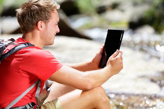 Tablet computer man hiker hiking in Yosemite, USA using travel app or map during hike, resting by river. Caucasian male hiker relaxing on a summer day.