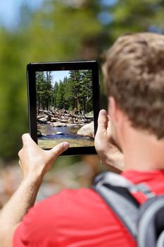 Hiking hiker man taking pictures of forest on digital tablet computer. Young adult doing mobile photography of nature landscape in Yosemite National Park, California, USA.