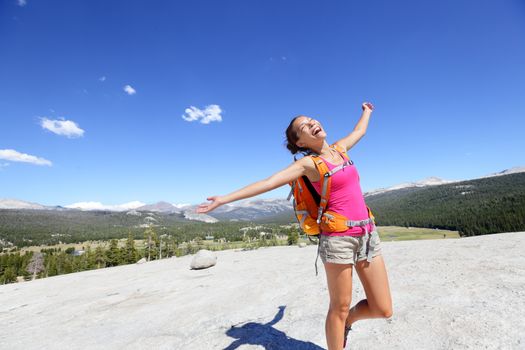 Happy hiking woman dancing in mountain landscape. Young asian adult doing funny freedom pose on top of the Pothole Dome in Yosemite National Park, California, USA.