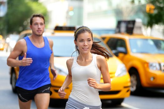 Active couple running on famous shopping street fifth avenue in Manhattan, New York City NYC, USA. Exercise lifestyle portrait of young asian woman runner and caucasian male jogger.