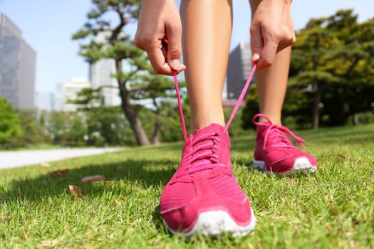 Runner getting ready for jogging tying running shoes laces - Woman preparing before run putting on trainers in japanese park near Ginza in Tokyo, Japan