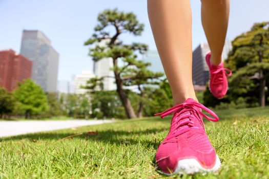 Running shoes - woman runner jogging staying fit in Tokyo Park, Japan. Closeup of pink trainers in green grass in summer park near the Imperial Palace and Ginza district downtown.