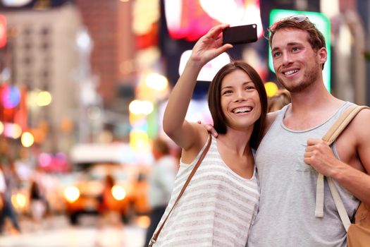 Travel tourist couple taking selfie with smartphone in New York City, USA. Self-portrait photo on Times Square at night. Beautiful young tourists having fun, Manhattan, USA. Asian woman, Caucasian man