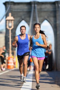 New York runners running training on Brooklyn bridge NYC during busy rush hours with tourists. Fit young couple doing their workout routine on a summer day.