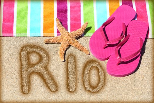 Rio beach concept. Overhead view ot the word RIO written on golden sand with a starfish, pink flip flops and towel conceptual of a summer vacation and travel in Rio de Janiero, Brazil